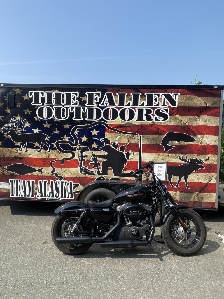 The Fallen Outdoors Team Alaska sign next to a motorcycle